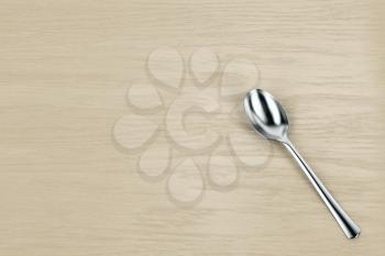 Silver spoon on wooden table, top view