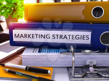 Blue Office Folder with Inscription Marketing Strategies on Office Desktop with Office Supplies and Modern Laptop. Marketing Strategies Business Concept on Blurred Background. 3D Render.