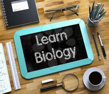 Learn Biology Handwritten on Mint Small Chalkboard. Top View of Wooden Office Desk with a Lot of Business and Office Supplies on It. Small Chalkboard with Learn Biology. 3d Rendering.