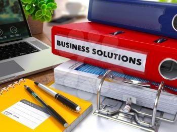 Red Ring Binder with Inscription Business Solutions on Background of Working Table with Office Supplies, Laptop, Reports. Toned Illustration. Business Concept on Blurred Background.