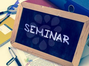 Seminar - Handwritten by white Chalk on a Blackboard. Composition with Small Chalkboard on Background of Working Table with Office Folders, Stationery, Reports. Blurred Background. Toned Image.