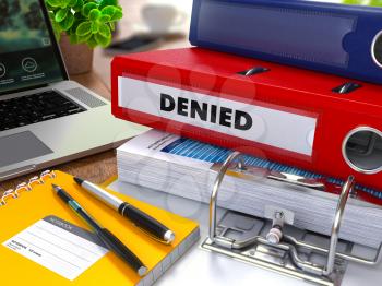 Red Ring Binder with Inscription Denied on Background of Working Table with Office Supplies, Laptop, Reports. Toned Illustration. Business Concept on Blurred Background.