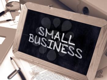 Handwritten Small Business on a Chalkboard. Composition with Chalkboard and Ring Binders, Office Supplies, Reports on Blurred Background. Toned Image.