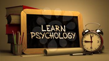 Handwritten Learn Psychology on a Chalkboard. Composition with Chalkboard and Stack of Books, Alarm Clock and Rolls of Paper on Blurred Background. Toned Image.