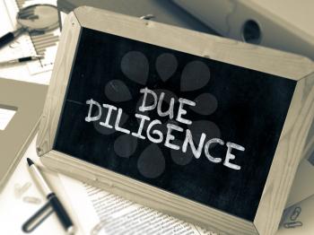 Due Diligence Handwritten on Chalkboard. Composition with Small Chalkboard on Background of Working Table with Ring Binders, Office Supplies, Reports. Blurred Background. Toned Image.