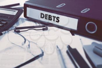 Debts - Office Folder on Background of Working Table with Stationery, Glasses, Reports. Business Concept on Blurred Background. Toned Image.