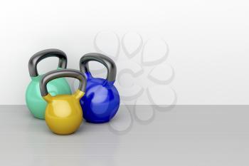 Three kettlebells of different size on shiny gray floor in the fitness center
