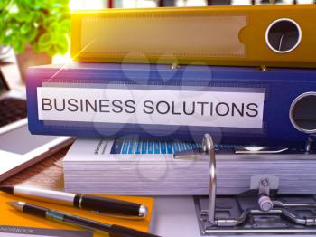 Blue Ring Binder with Inscription Business Solutions on Background of Working Table with Office Supplies and Laptop. Business Solutions Business Concept on Blurred Background. 3D Render.