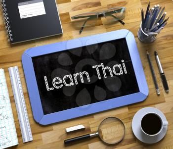 Learn Thai Handwritten on Blue Small Chalkboard. Top View of Wooden Office Desk with a Lot of Business and Office Supplies on It. Learn Thai on Small Chalkboard. 3d Rendering.