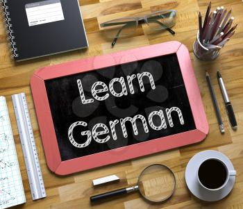 Learn German on Small Chalkboard. Learn German - Red Small Chalkboard with Hand Drawn Text and Stationery on Office Desk. Top View. 3d Rendering.
