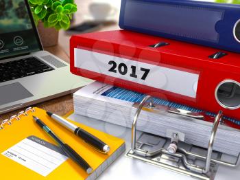 Red Ring Binder with Inscription 2017 on Background of Working Table with Office Supplies, Laptop, Reports. Toned Illustration. Business Concept on Blurred Background.