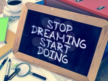 Stop Dreaming Start Doing. Motivational Quote Hand Drawn on Chalkboard on Working Table Background. Blurred Background. Toned Image.