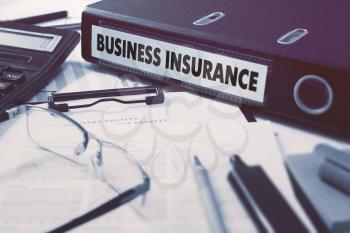 Ring Binder with inscription Business Insurance on Background of Working Table with Office Supplies, Glasses, Reports. Toned Illustration. Business Concept on Blurred Background.