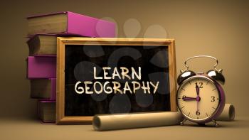 Learn Geography - Chalkboard with Hand Drawn Inspirational Quote, Stack of Books, Alarm Clock and Rolls of Paper on Blurred Background. Toned Image.