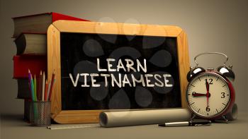 Learn Vietnamese - Chalkboard with Hand Drawn Motivational Quote, Stack of Books, Alarm Clock and Rolls of Paper on Blurred Background. Toned Image.