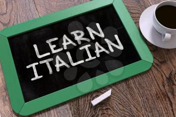 Learn Italian - Green Chalkboard with Hand Drawn Text and White Cup of Coffee on Wooden Table. Top View.