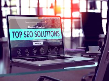Top SEO - Search Engine Optimization - Solutions Concept. Closeup Landing Page on Laptop Screen  on background of Comfortable Working Place in Modern Office. Blurred, Toned Image.