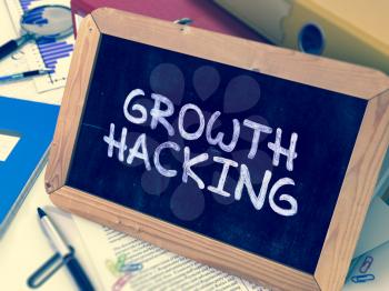 Handwritten Growth Hacking on a Chalkboard. Composition with Chalkboard and Ring Binders, Office Supplies, Reports on Blurred Background. Toned 3d Image.